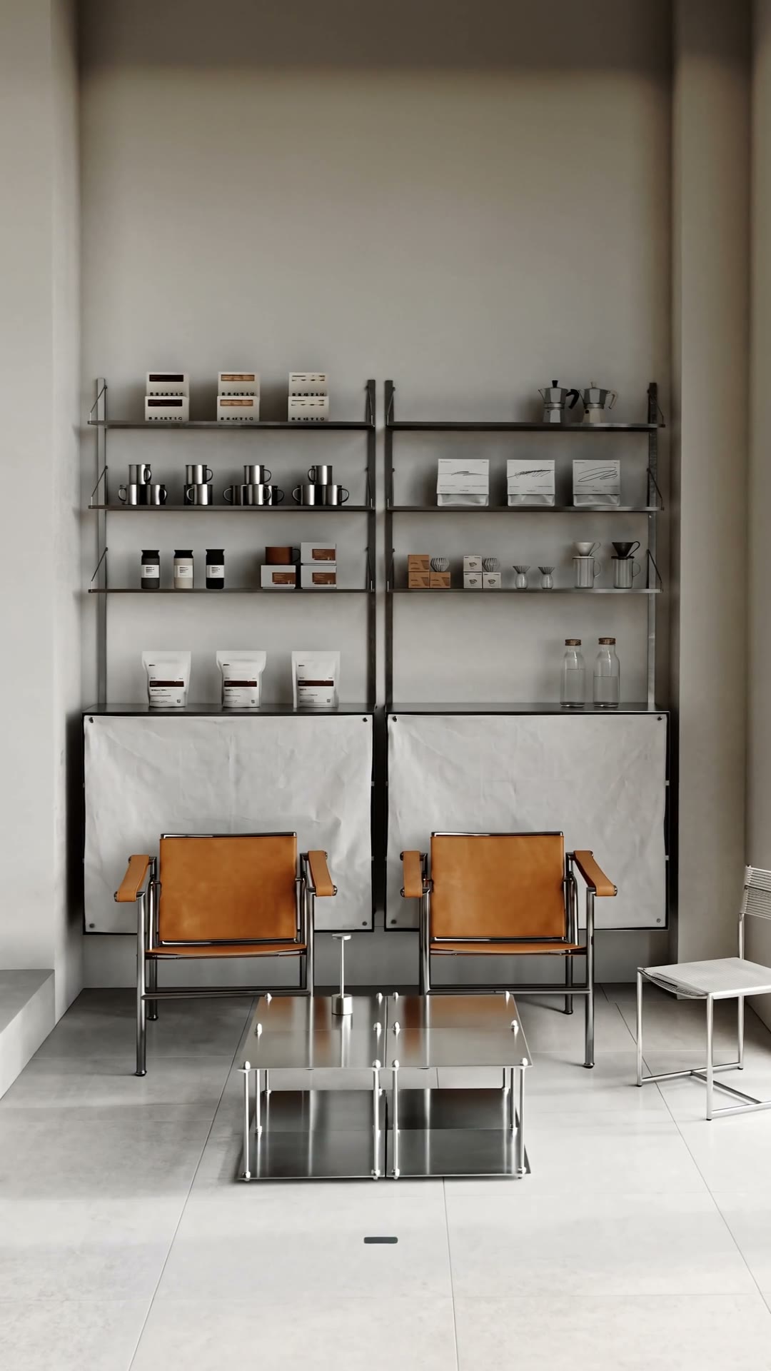 A minimalist lounge with two leather armchairs, a steel side table and shelves of coffee products
