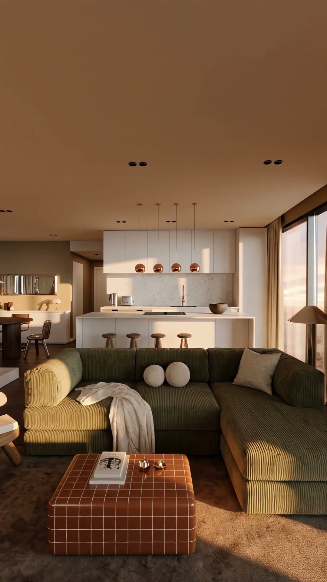 An open-plan living room and kitchen at golden hour with a green corduroy sofa and a tiled ottoman